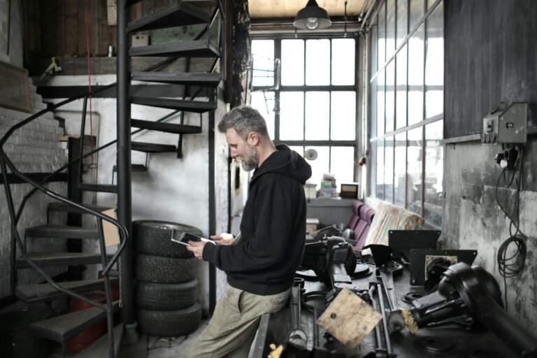 Bearded worker using tablet while standing near workbench in workshop